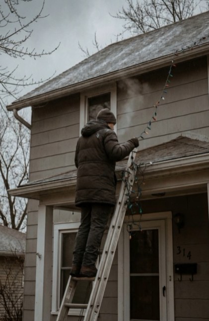 Climbing a ladder to hang holiday lights in the cold